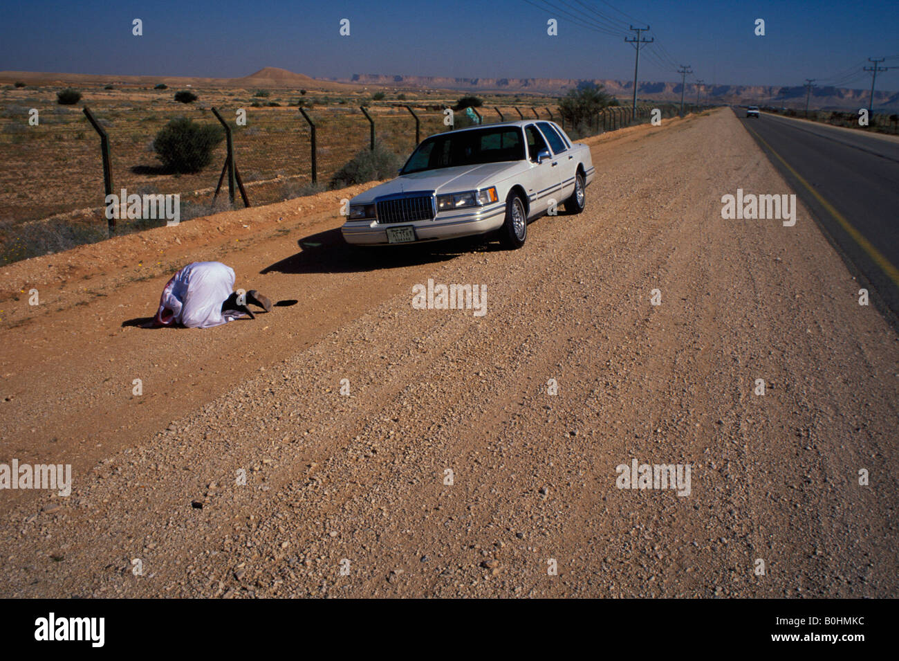 Un homme qui prie par une voiture au bord de la route, l'Arabie Saoudite. Banque D'Images
