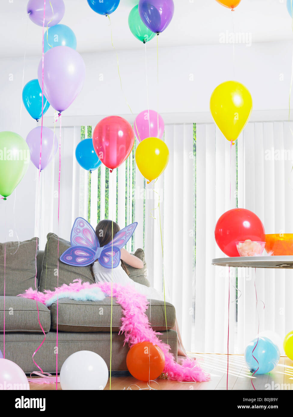 Jeune fille (7-9) sitting on sofa with balloons, portant des ailes de fées, vue arrière Banque D'Images