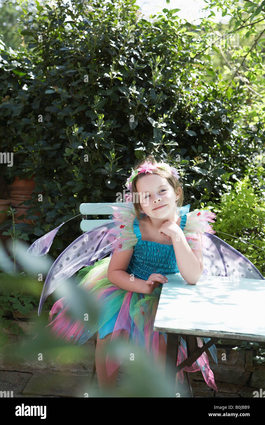 Portrait of young girl (5-6) in fairy costume assis à table de jardin Banque D'Images