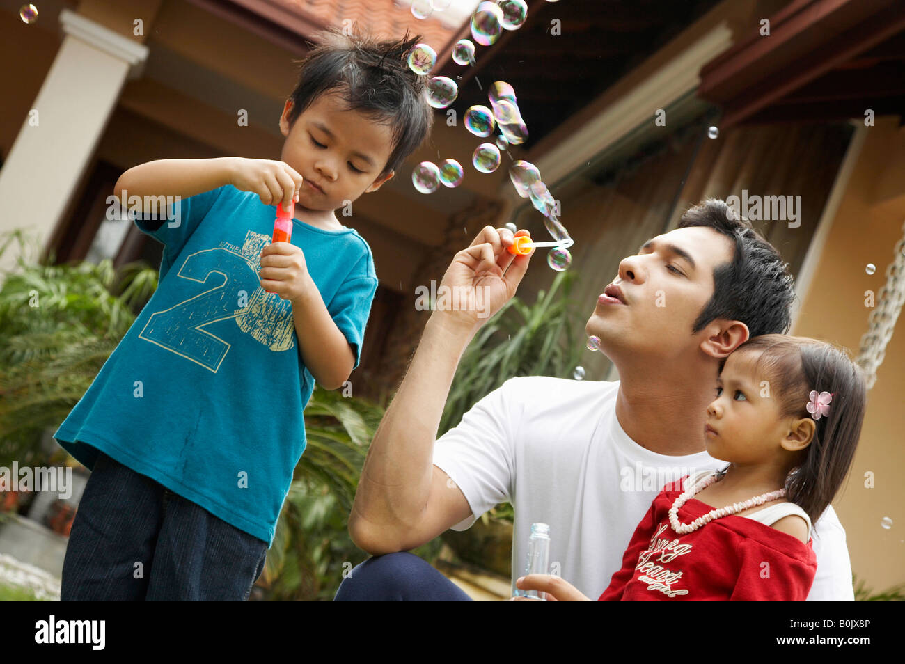 Père s'amusant avec ses deux enfants, soufflant des bulles de savon ensemble Banque D'Images