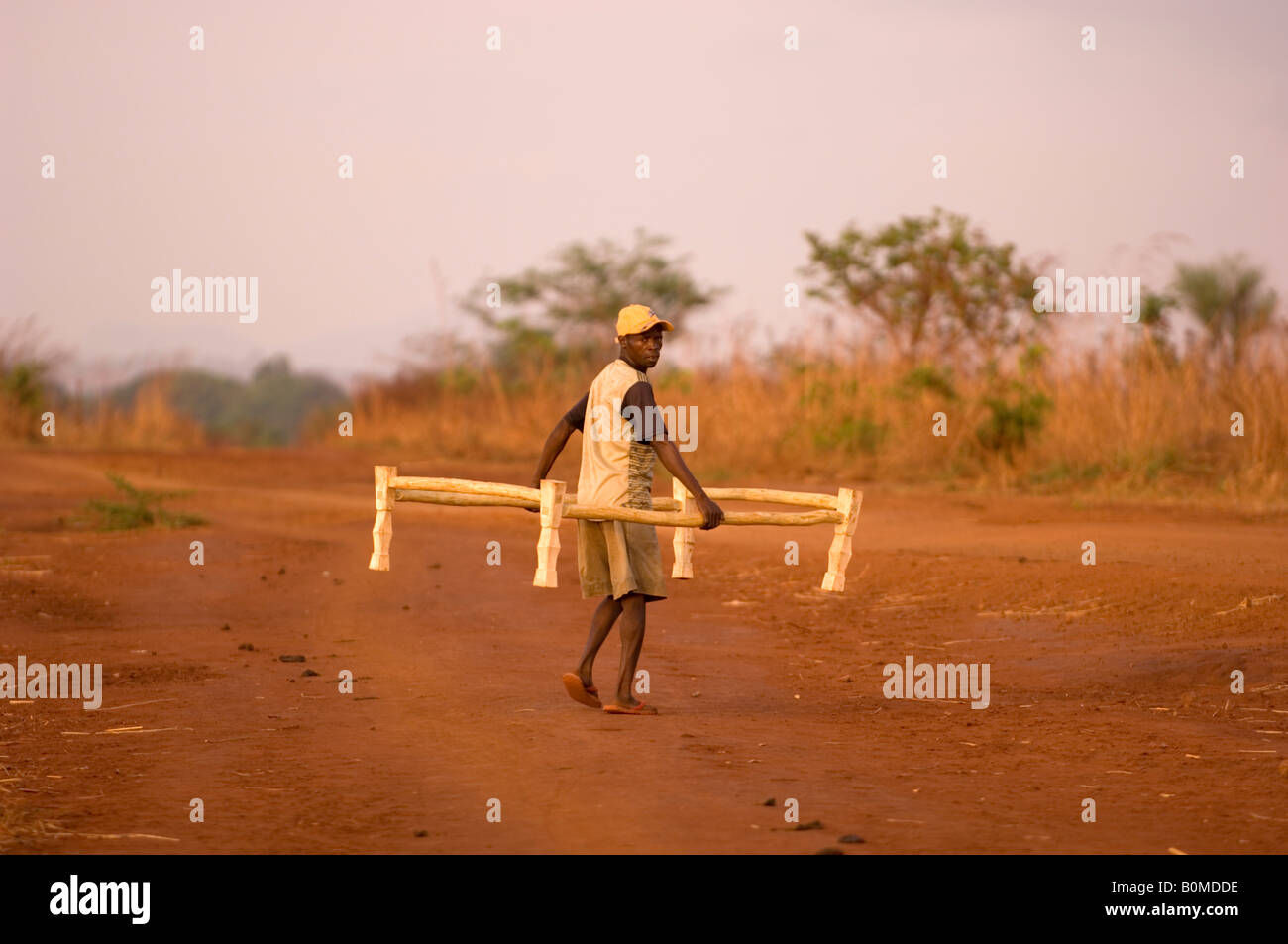 Personne mâle porte un cadre de lit sur un chemin de poussière rouge au Mozambique, l'Afrique. Banque D'Images