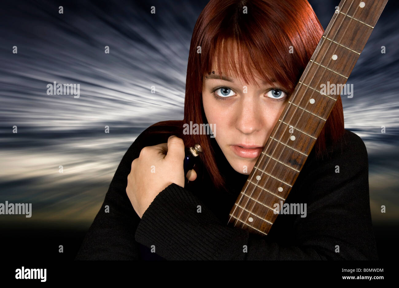 Jeune fille rousse déprimée protégeant sa guitare avec un arrière-plan dramatique Banque D'Images