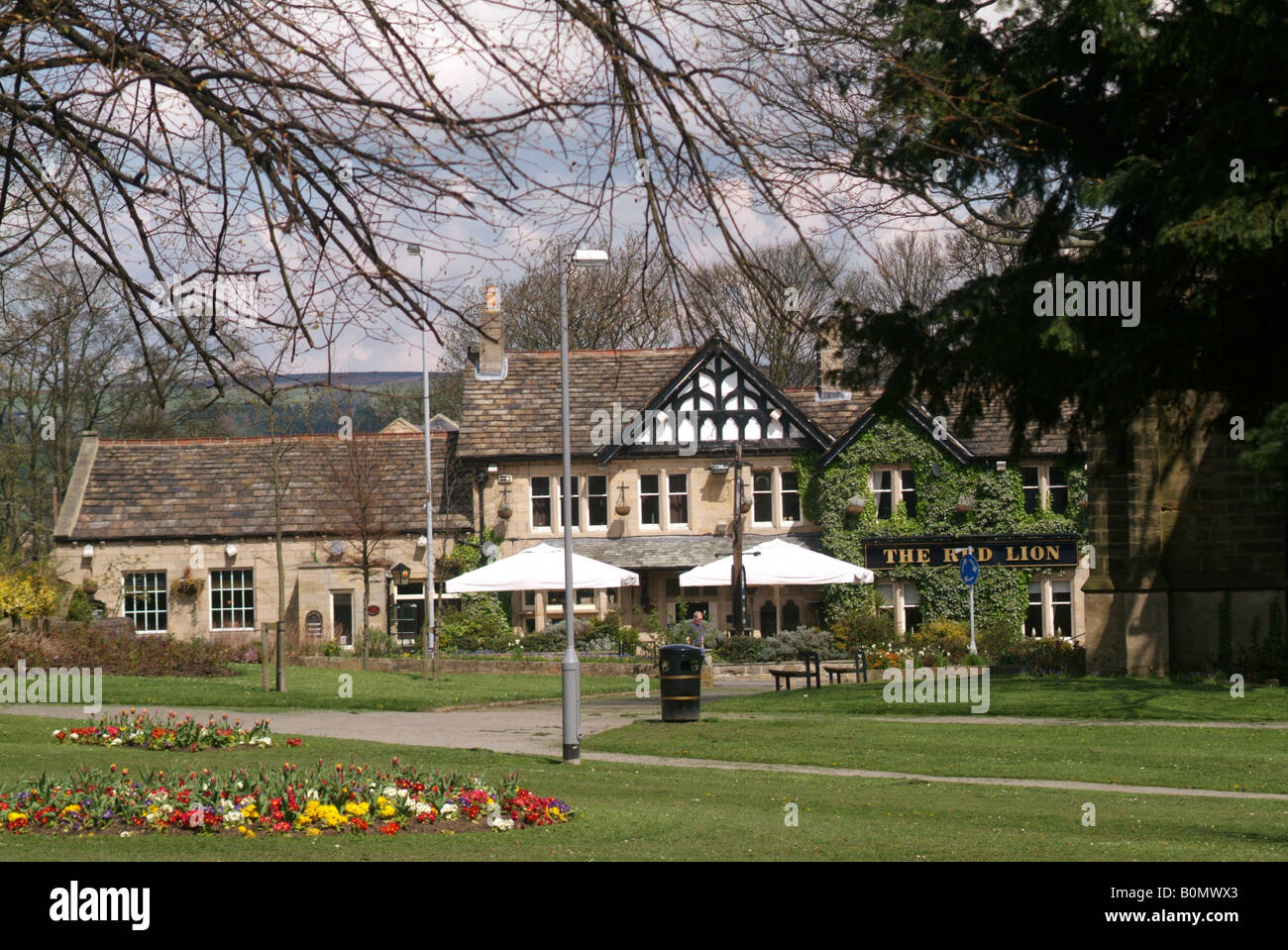 Le Red Lion Inn vu au-delà des fleurs et des espaces verts dans la rue principale de Burley dans Wharfedale Banque D'Images