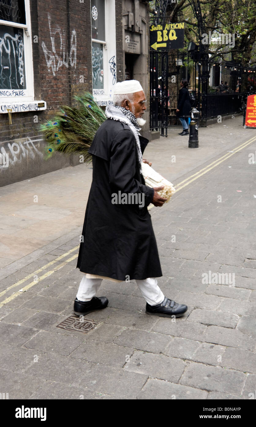 Bangladais âgés man crossing Brick Lane avec plumes de paon à vendre Banque D'Images