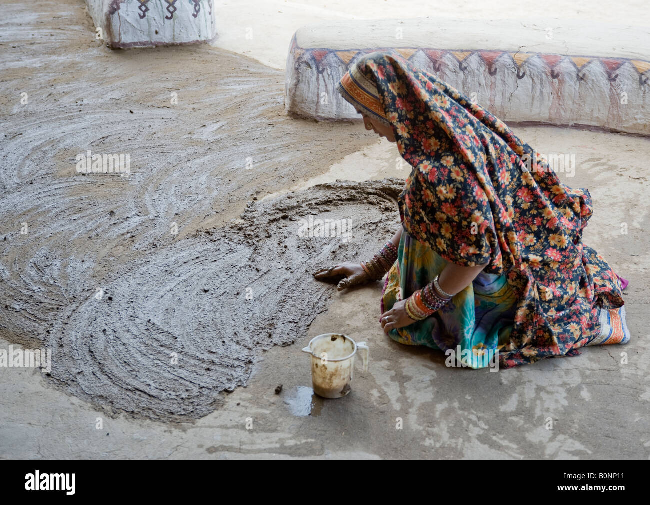 Femme indienne en costume national Katchi ciment cours propagation-mix sur le plancher de la réception d'une station de vacances safari dans le désert. Banque D'Images