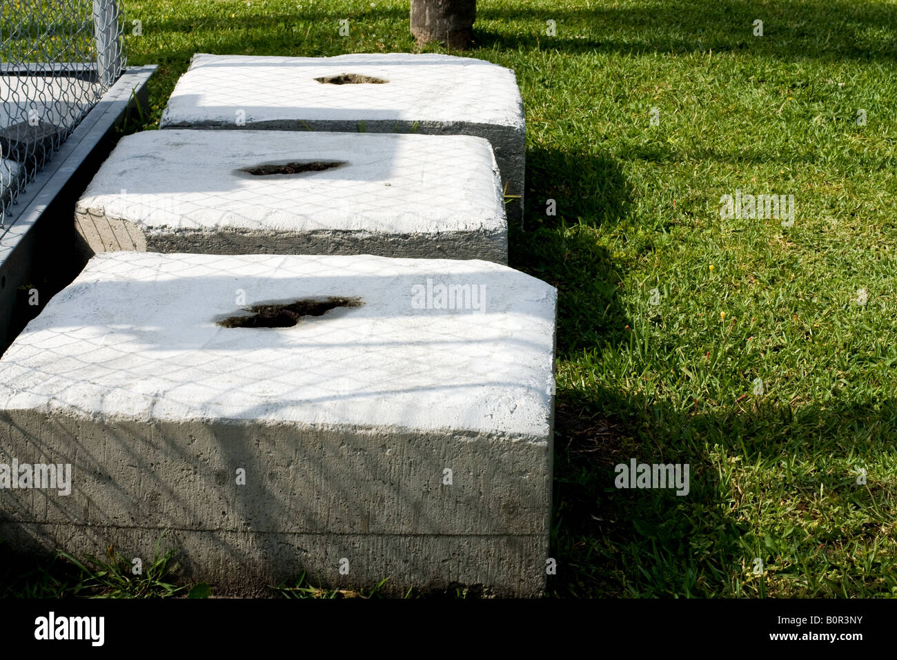 Trois blocs de béton avec des trous irréguliers dans le milieu de l'herbe à côté d'une clôture Banque D'Images