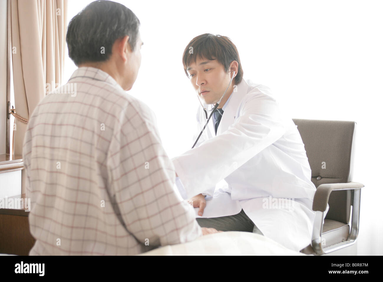Homme médecin examinant homme plus âgé avec stéthoscope dans nursing home Banque D'Images