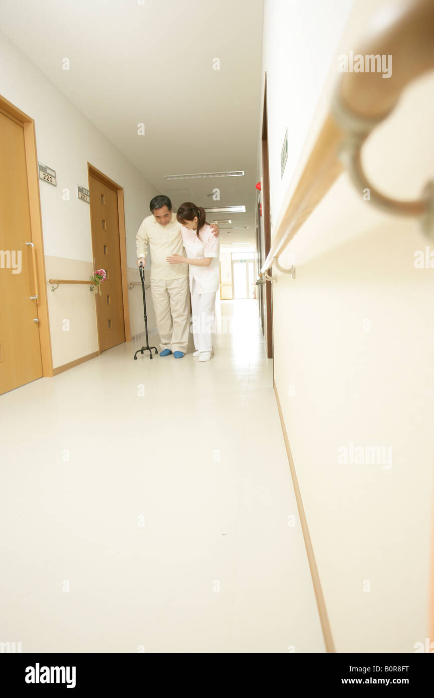 Nurse helping senior man walking in corridor Banque D'Images