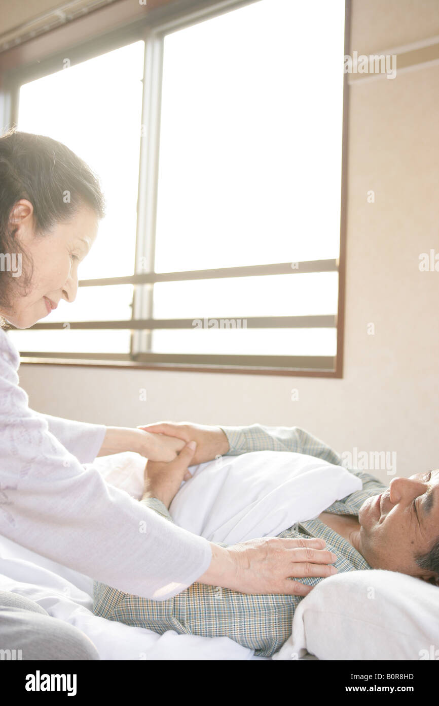 Senior woman sitting next to man in hospital bed Banque D'Images