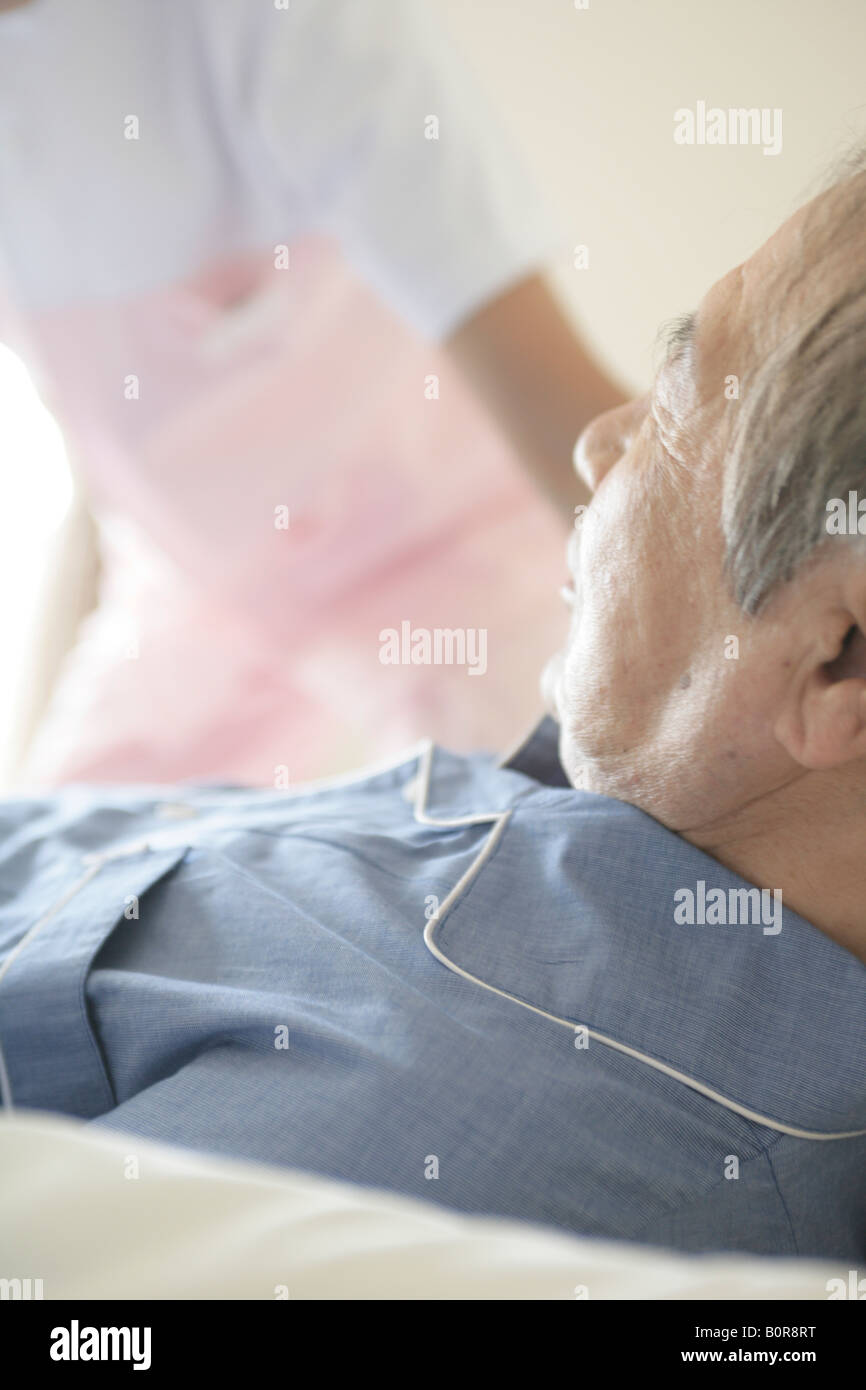 Man Lying in Bed, infirmière en arrière-plan Banque D'Images