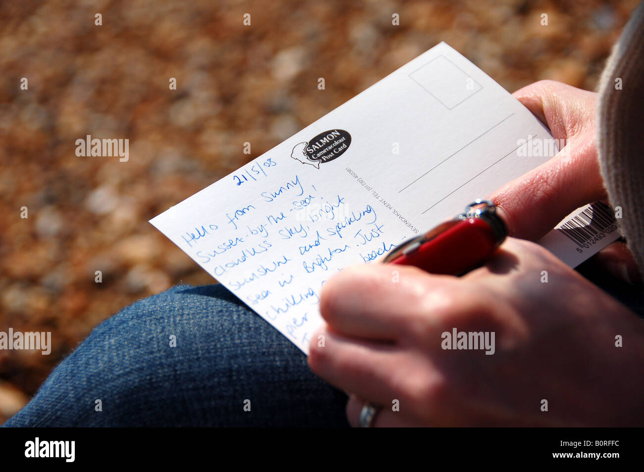 Femme écrivant une carte postale sur la plage, Brighton, UK Banque D'Images
