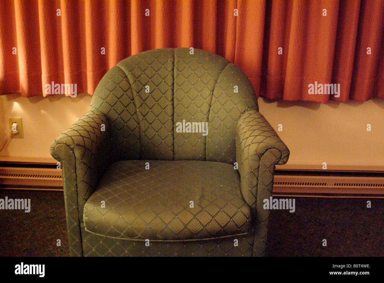 Chaise art déco verte dans la chambre de motel, avec rideaux rouges, chauffage par radiateur en plinthe et moquette mur à mur. Banque D'Images