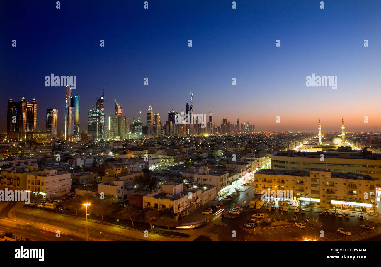 View vers le gratte-ciel sur la route Sheikh Zayed (L) et une mosquée illuminée au crépuscule à Dubaï, Émirats arabes unis. Banque D'Images