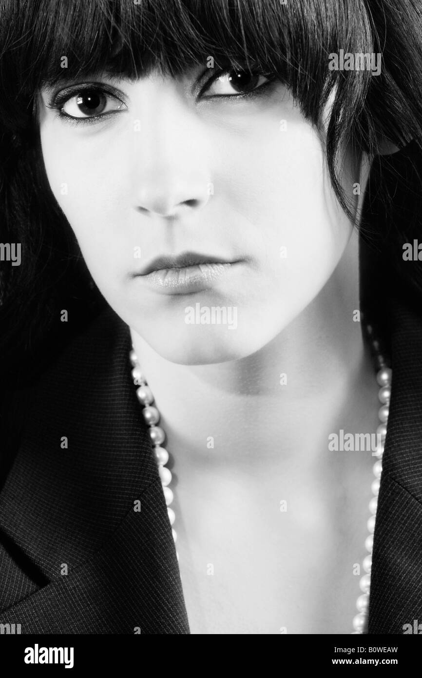 Portrait d'une fille aux cheveux noirs et de grands yeux portant un collier de perle, noir et blanc Banque D'Images
