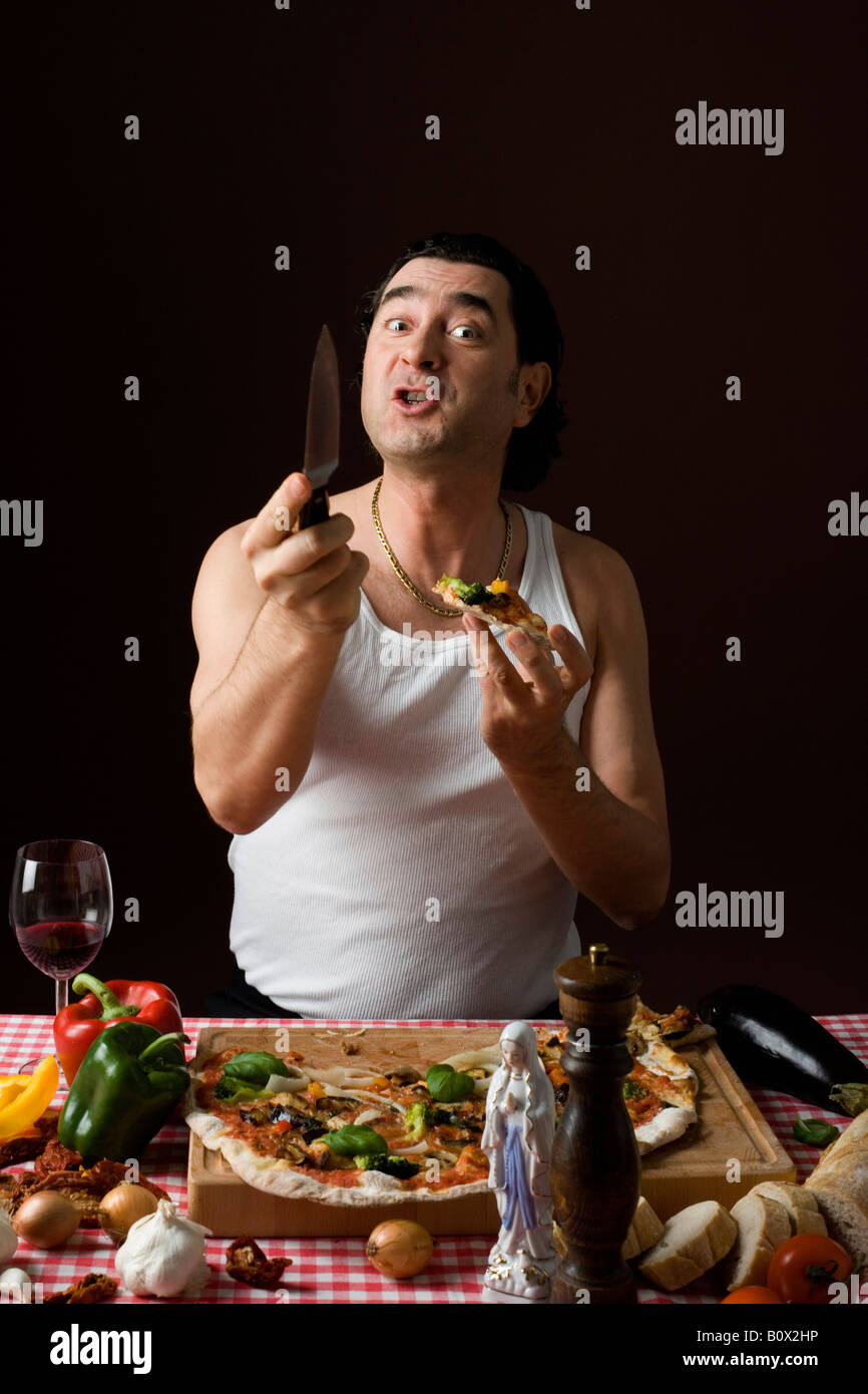 Man eating pizza italienne stéréotypées et tenant un couteau agressive Banque D'Images