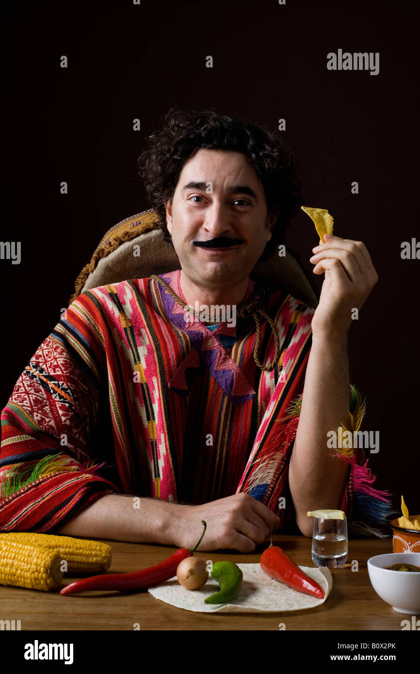 Les stéréotypes homme mexicain avec ingrédients mexicains manger une tortilla chip Banque D'Images