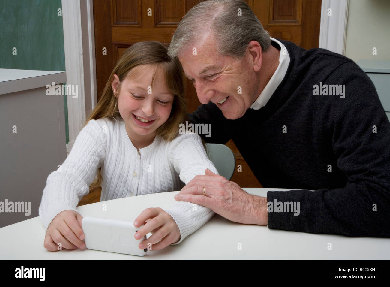 Une petite-fille à l'aide d'un appareil électronique pendant que son grand-père watch Banque D'Images