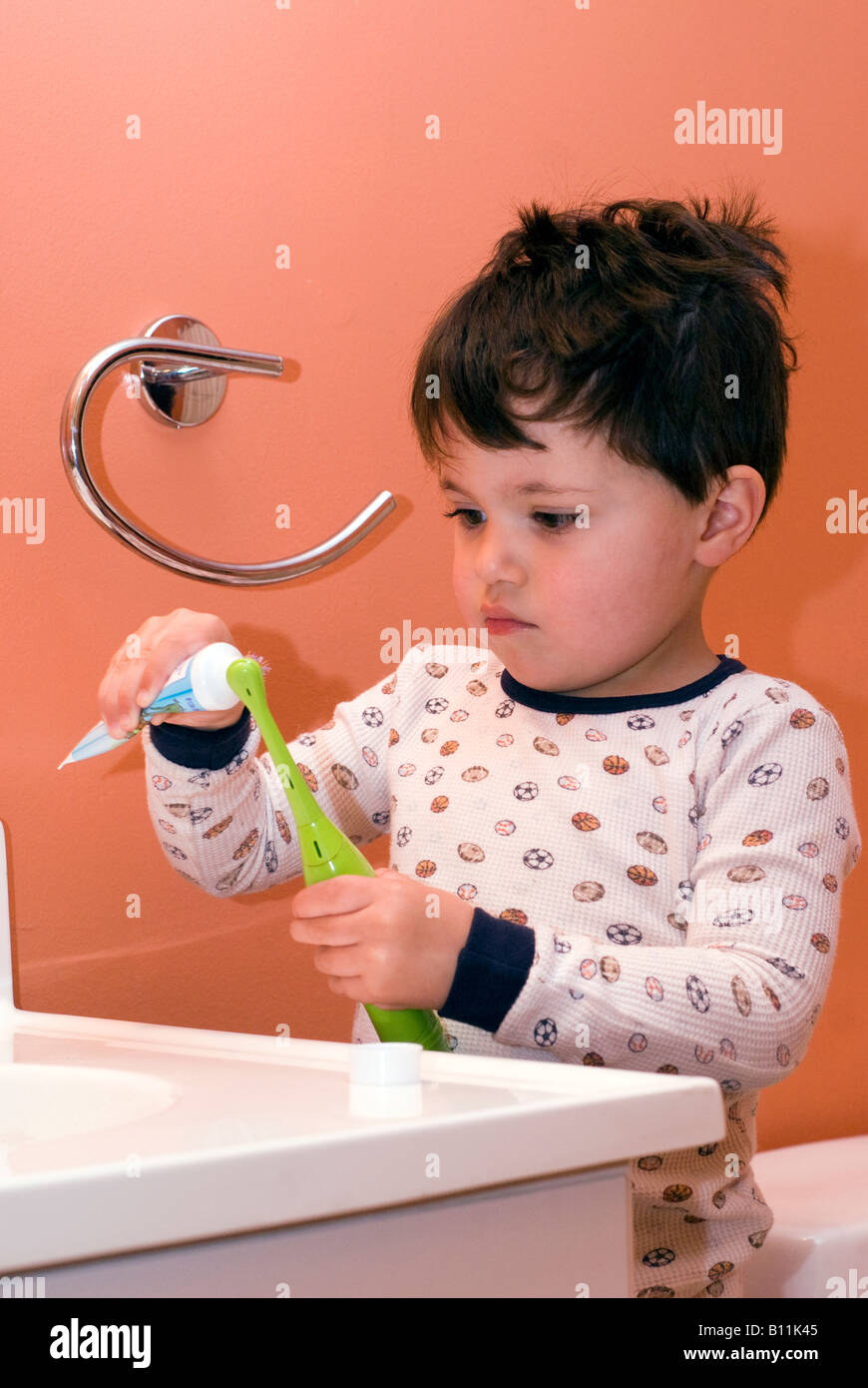 Deux et 1/2 ans garçon essaie de se brosser les dents tout seul avant qu'il se met au lit Banque D'Images