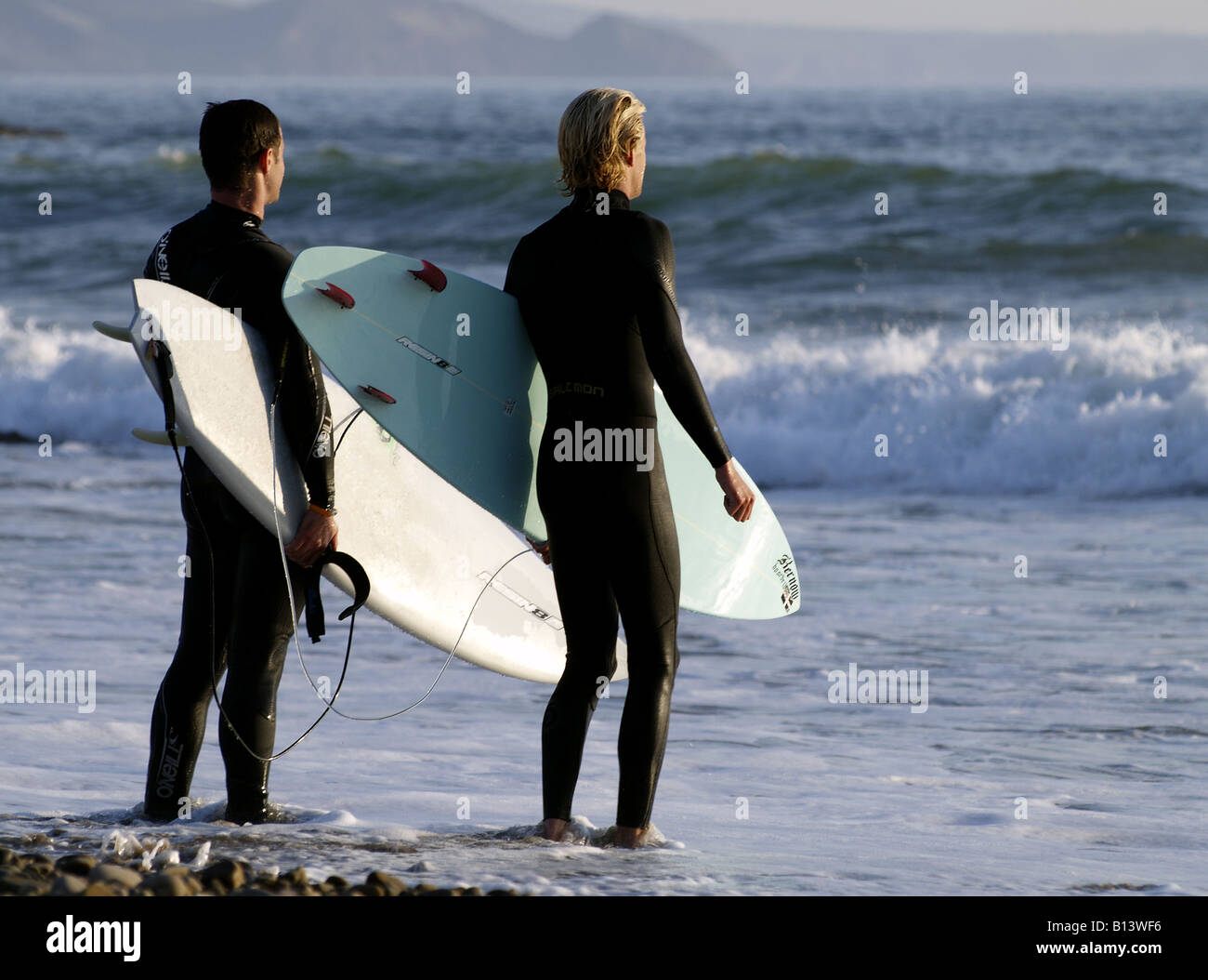 Deux surfeurs regardant les vagues en début de soirée à la plage de Crooklets, Bude, Cornwall, UK Banque D'Images