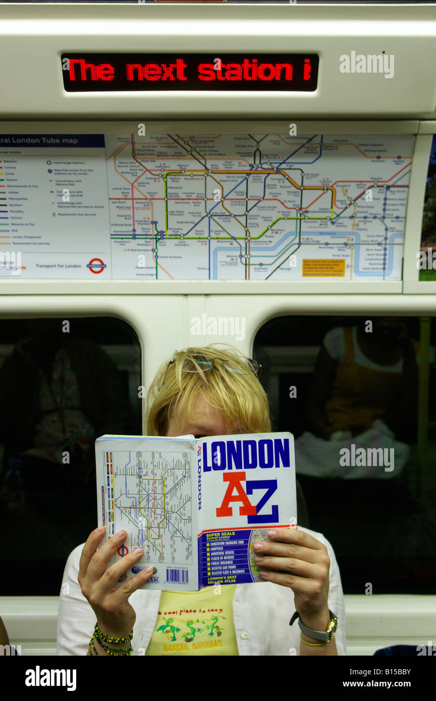 Jeune fille blonde woman tourist guide de lecture livre dans London Underground tube map sitting voyager Banque D'Images