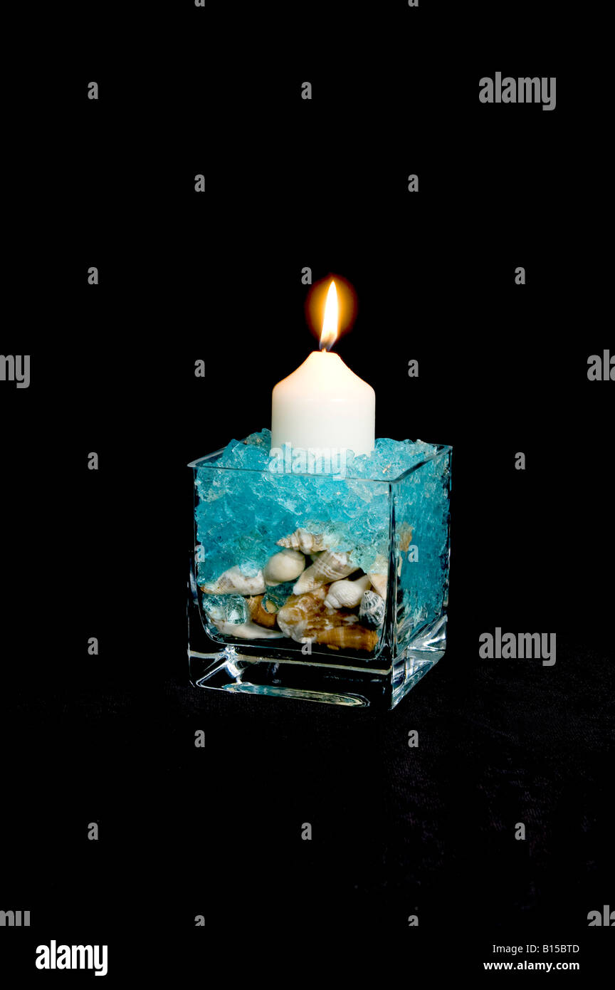 Cube en verre affichage de coquilles et de cristaux de gel bleu avec une bougie Banque D'Images