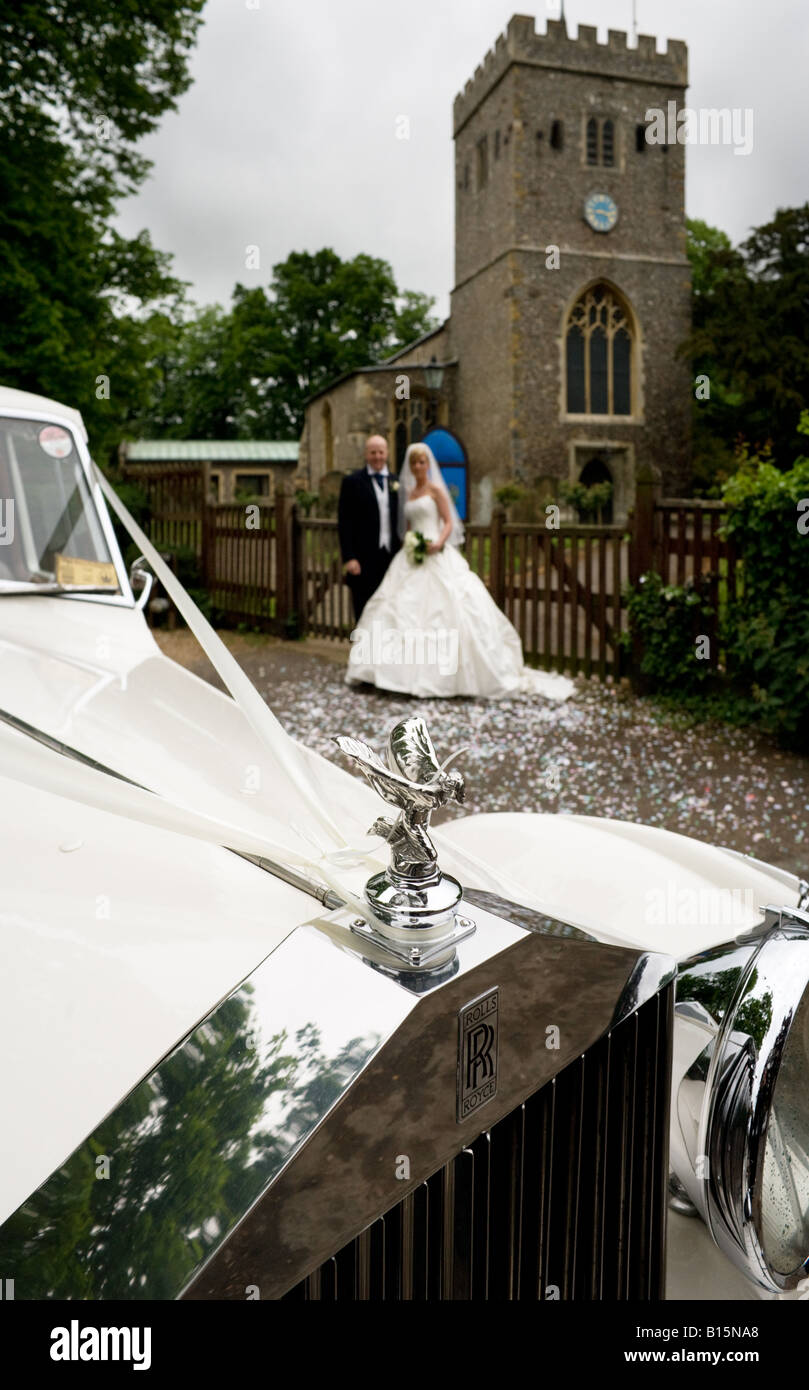 Mariée et le marié à l'extérieur de l'église paroissiale de Denham avec la voiture au premier plan suite nuptiale Banque D'Images