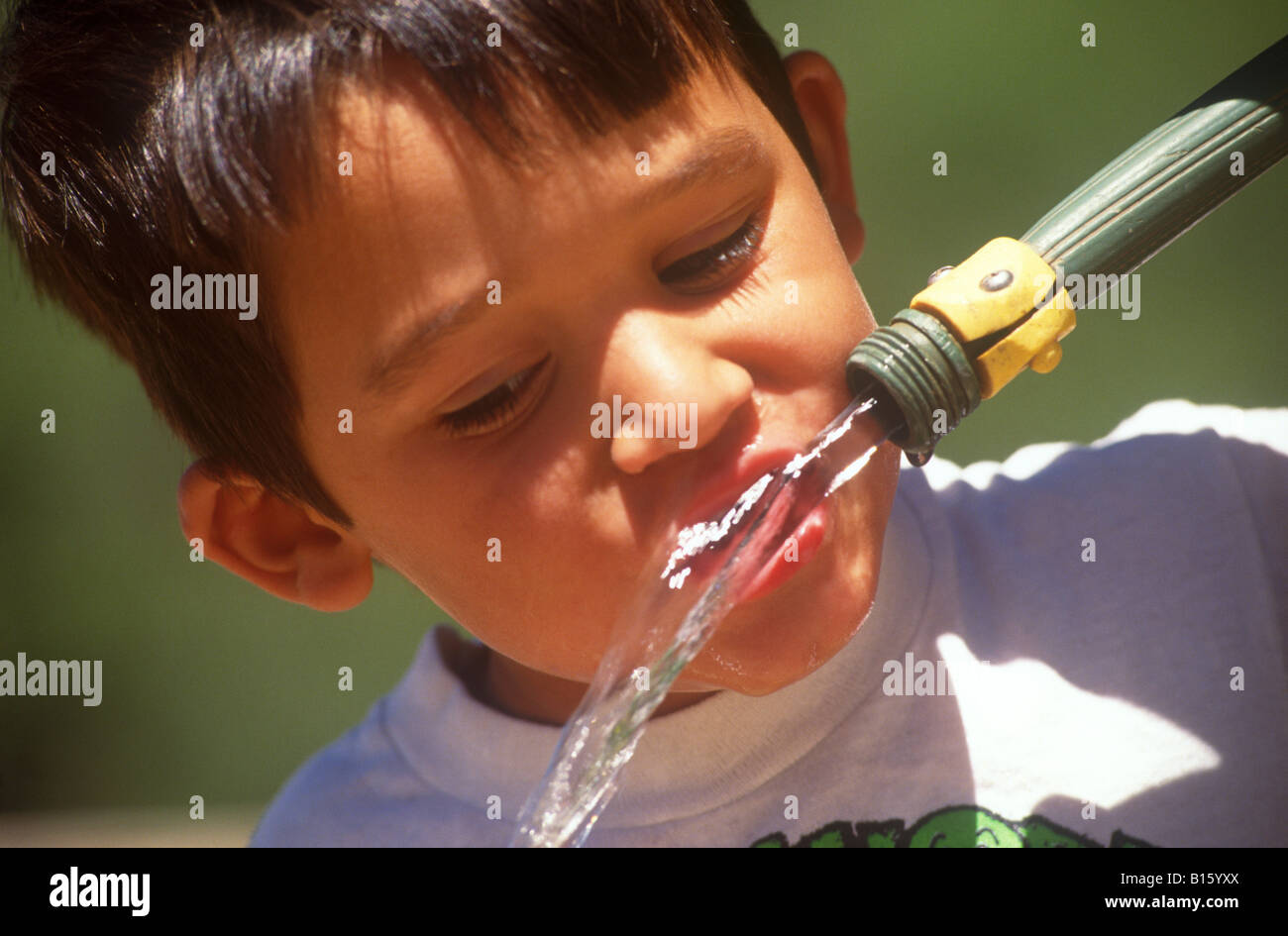 Boy boit de l'eau d'un tuyau de jardin. Banque D'Images