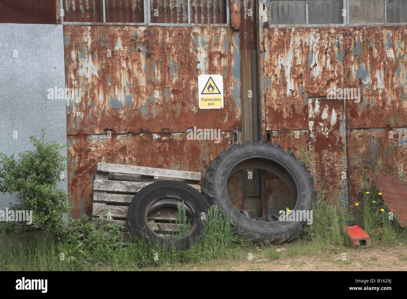 Les vieux pneus rusty portes de grange et des objets de la ferme avec panneau d'avertissement pour les gaz inflammables Banque D'Images