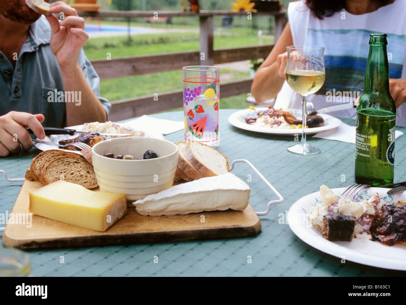 Close-up de fromage et de la nourriture sur table patio extérieur, avec deux personnes à manger l'arrière-plan Banque D'Images