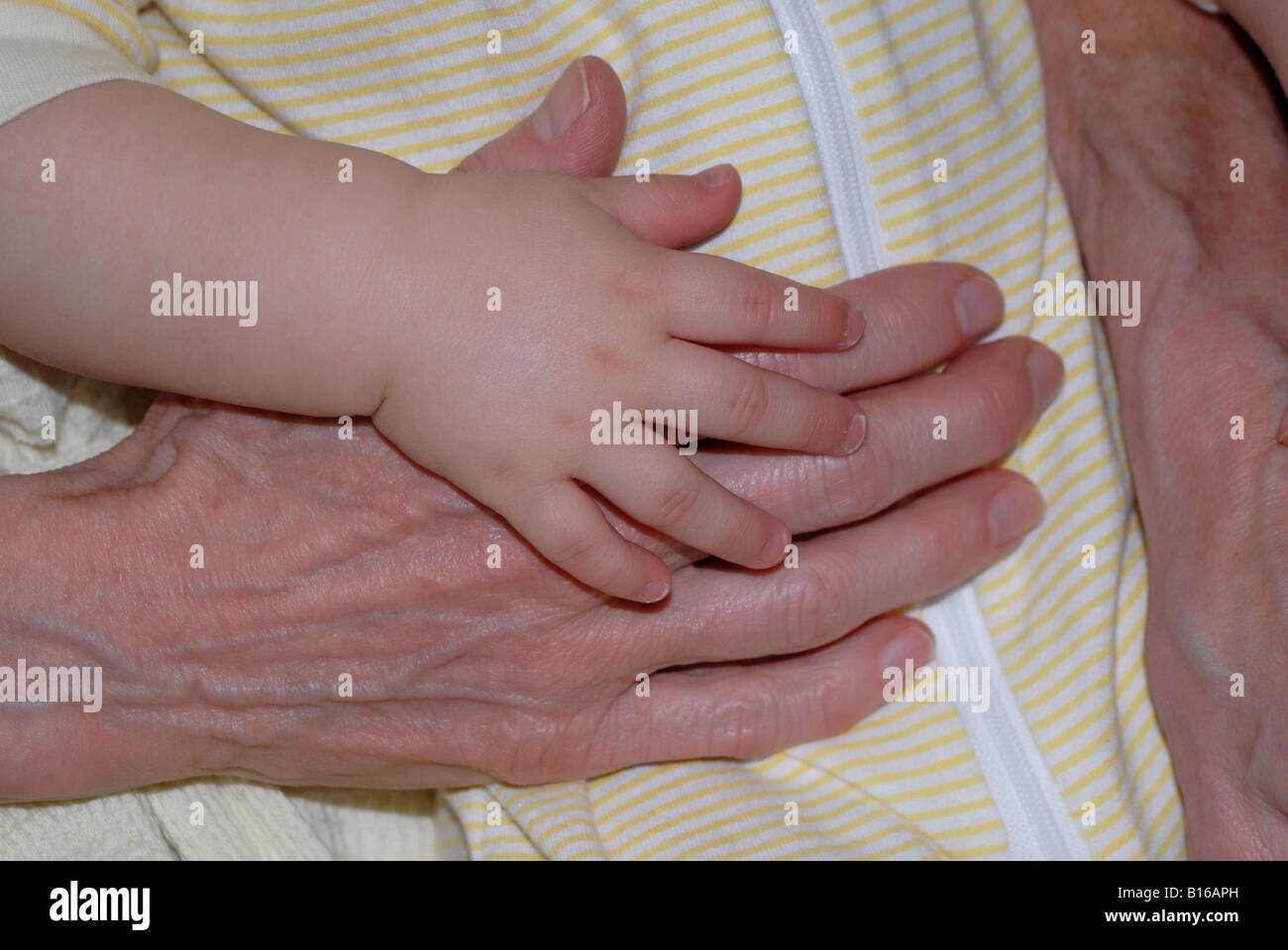 Une petite fille de 5 mois dort dans les bras de sa grand-mère tout en se tenant la main. Banque D'Images