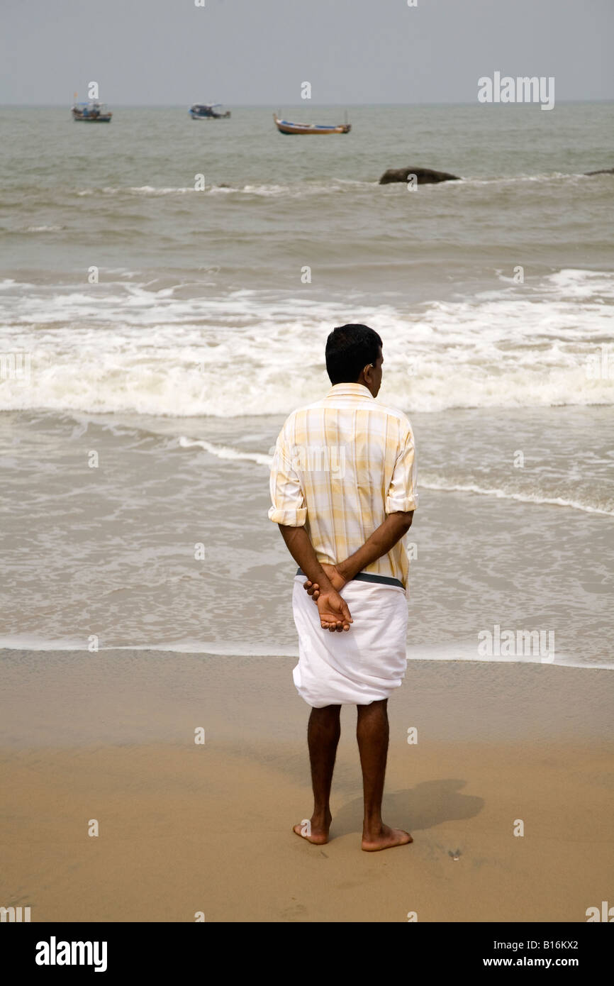 Kappil Beach à Kasaragod, Kerala. Un homme dans un dhoti se tient sur le sable et regarde les bateaux de pêche posés sur la mer d'Oman. Banque D'Images
