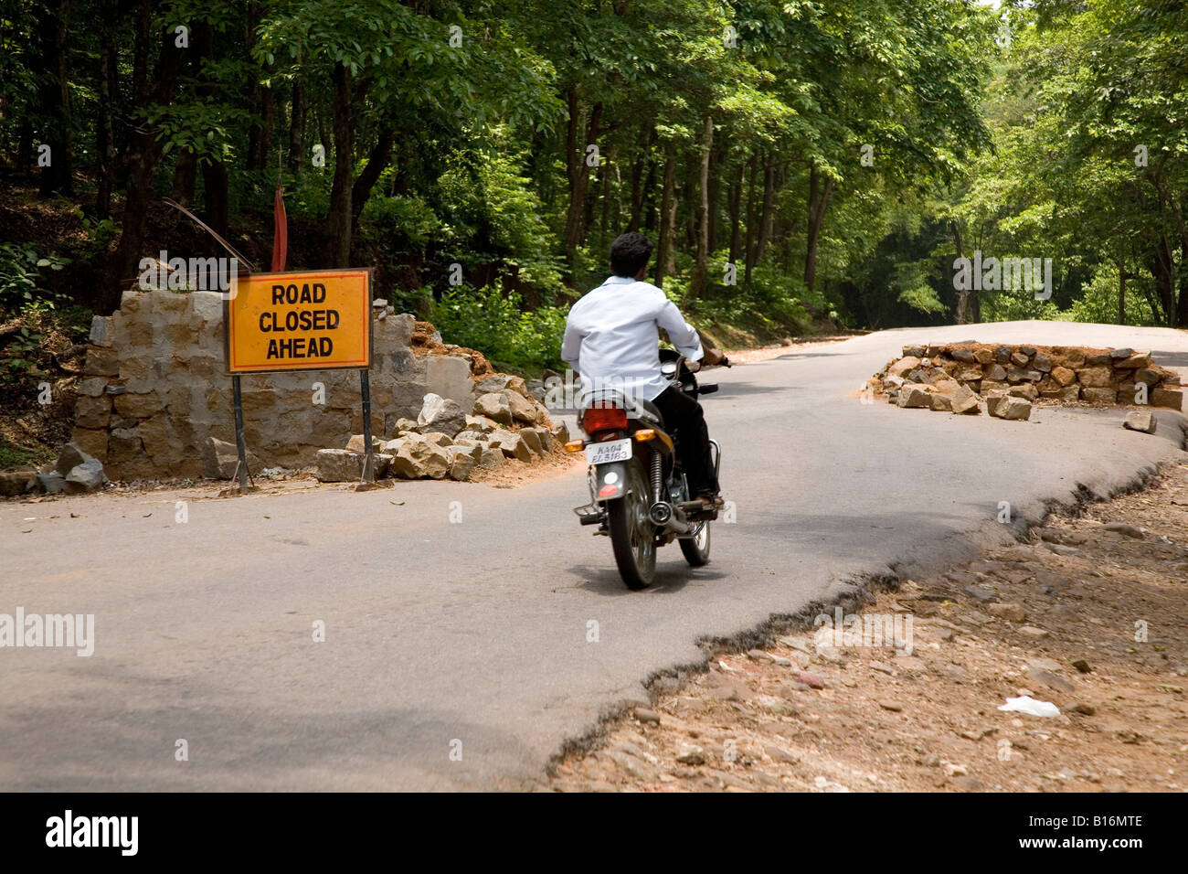 Un homme ignore un road closed sign à conduire à travers la forêt des Ghâts occidentaux sur l'Bangalore-Mangalore route nationale. Banque D'Images