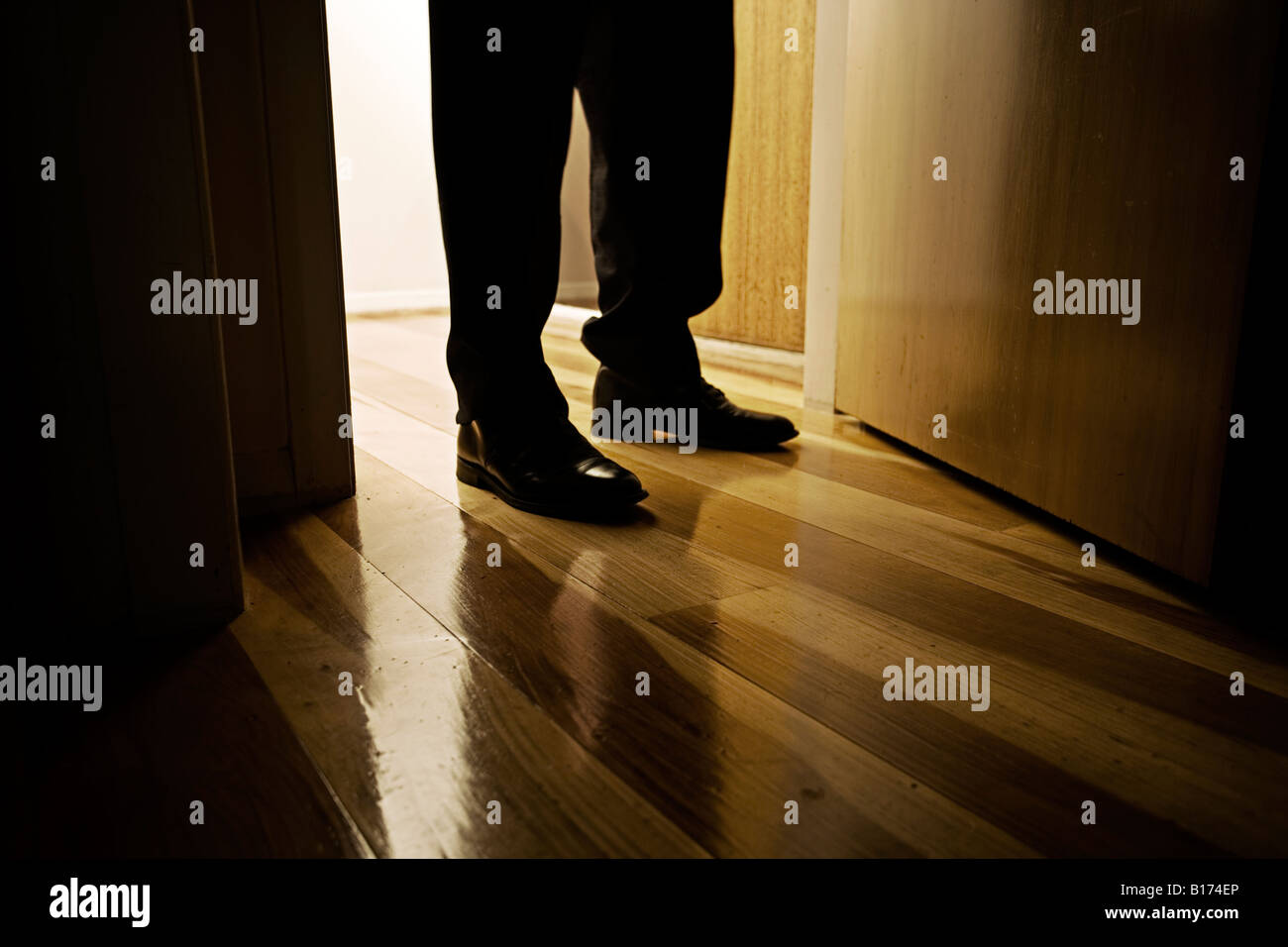 Les pieds de l'homme chaussures en cuir noir debout dans un intérieur de porte avec plancher en bois Banque D'Images
