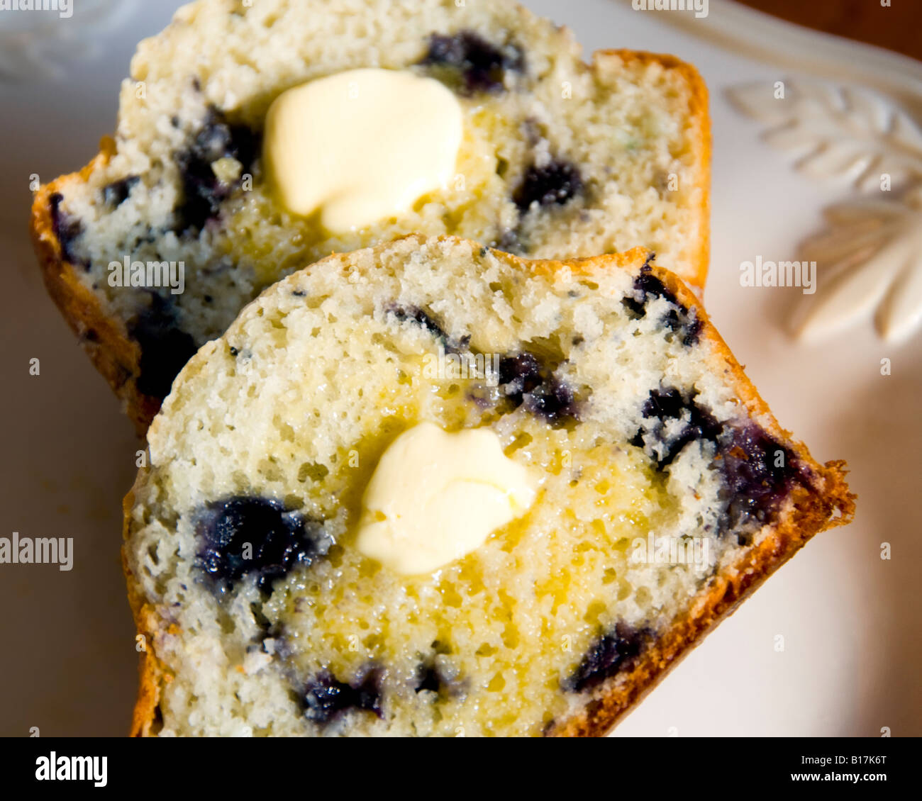 Un muffin aux bleuets, chaud du four, les couper en deux avec du beurre fondant sur chaque pièce. Banque D'Images
