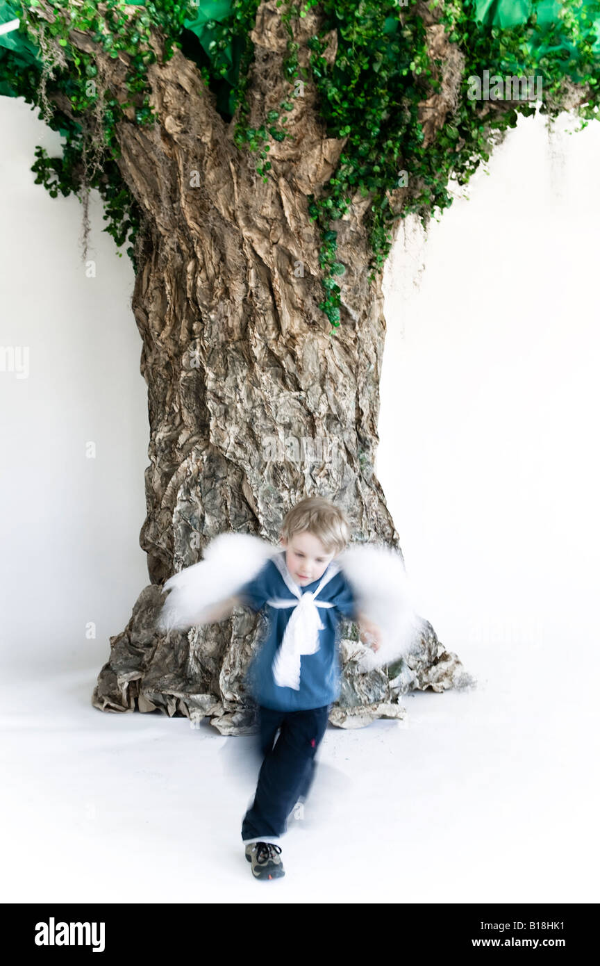 4 ans caucasien boy wearing angel wings running autour d'un faux arbre de papier, Montréal, Québec, Canada. Banque D'Images