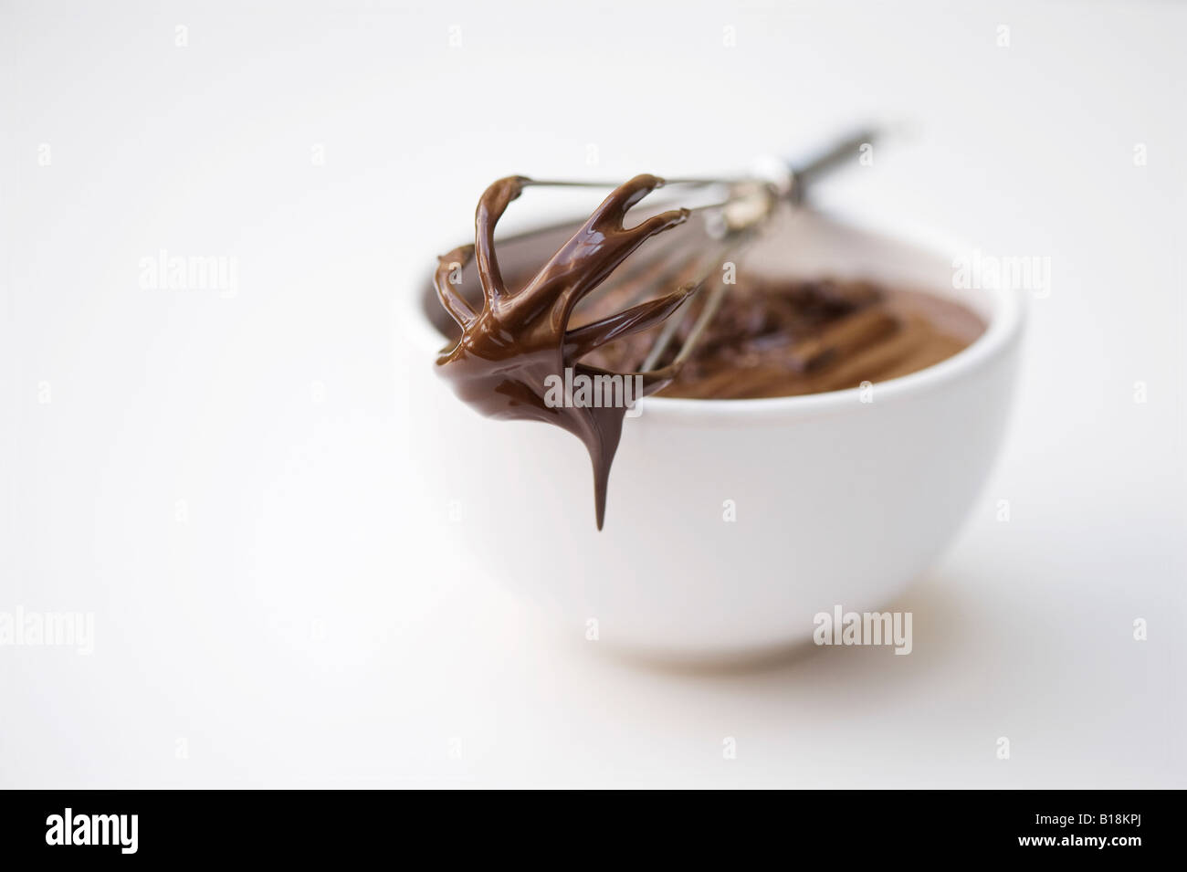Le chocolat dans un bol avec un fouet à main sur fond blanc Banque D'Images