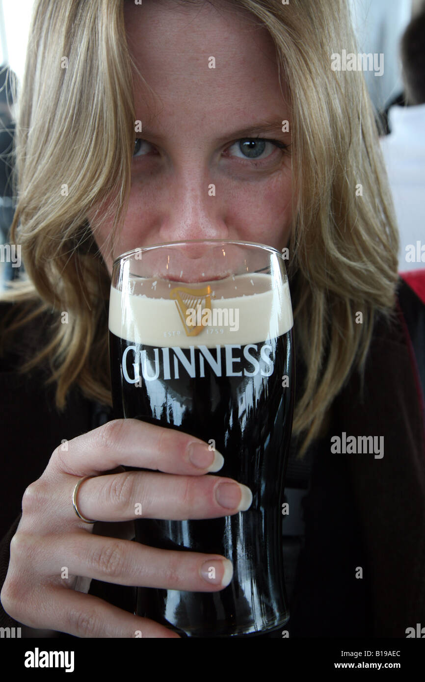 Femme profitant d'une pinte de bière Guinness à Dublin, Irlande — gros plan face derrière un verre de marque, tenue Patrick's Day Vibe. Banque D'Images
