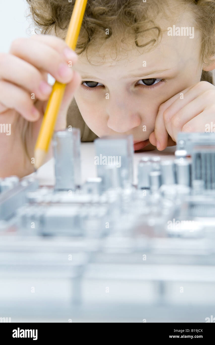 Little Boy looking at circuit board, holding pencil, close-up Banque D'Images