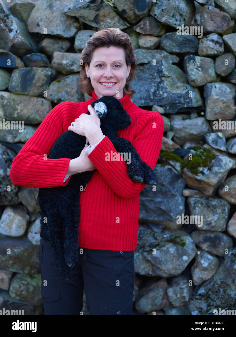 Sourire, femme de câliner bébé agneau noir sur ferme de moutons dans la région de Lake District Banque D'Images