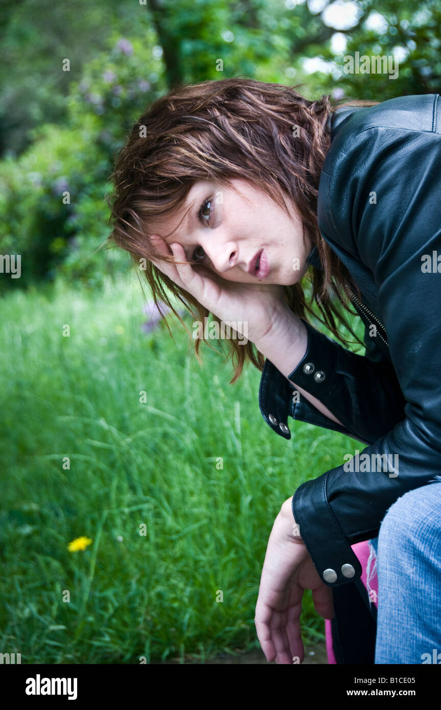 Jeune rousse red haired woman girl inquiets gueule anxieux déprimé triste solitaire seul assis à l'extérieur en tête du parc dans la main UK Banque D'Images