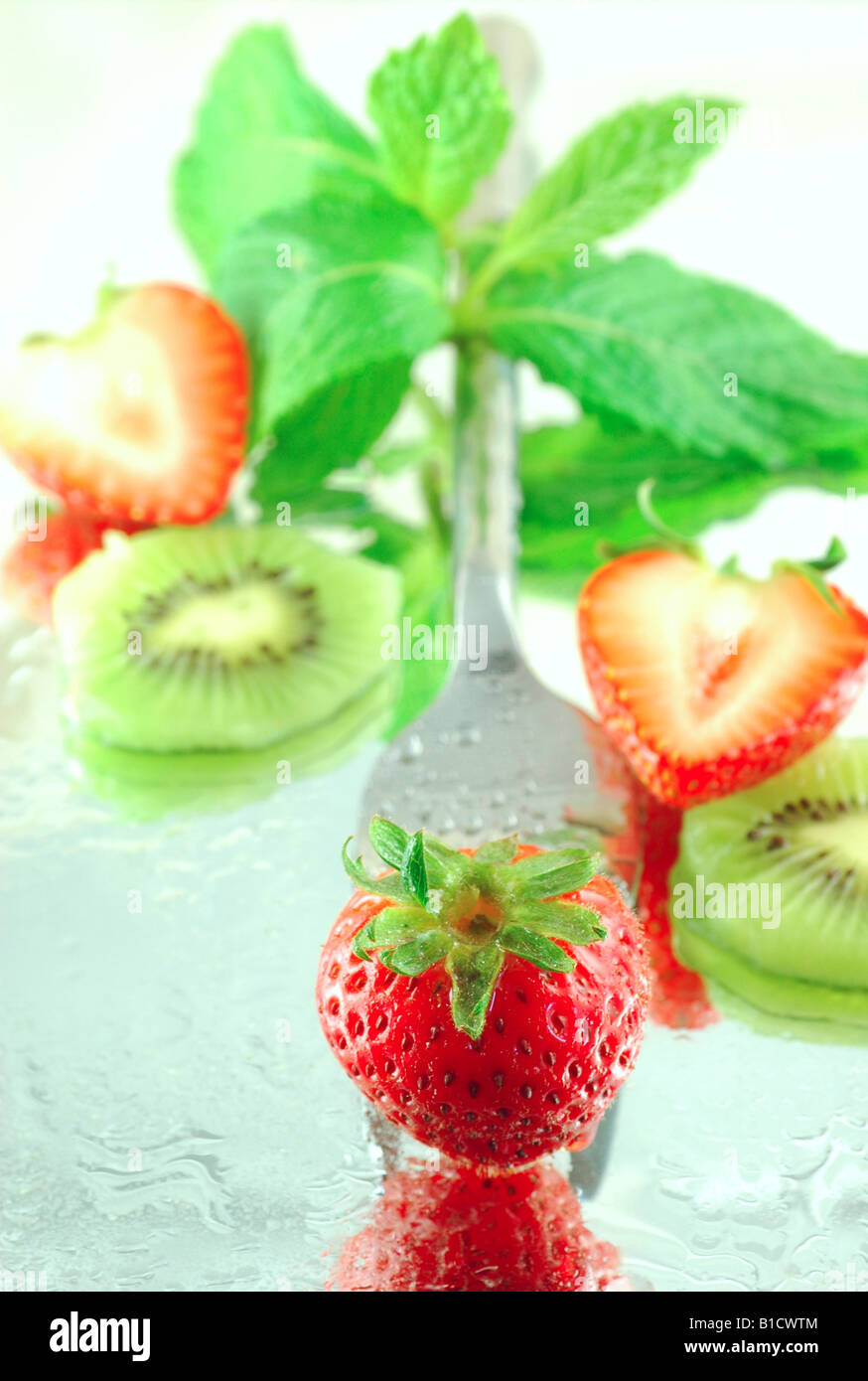 Les kiwis frais réfrigérés et les fraises à la menthe sur un fond réfléchissant avec une faible profondeur de champ Banque D'Images