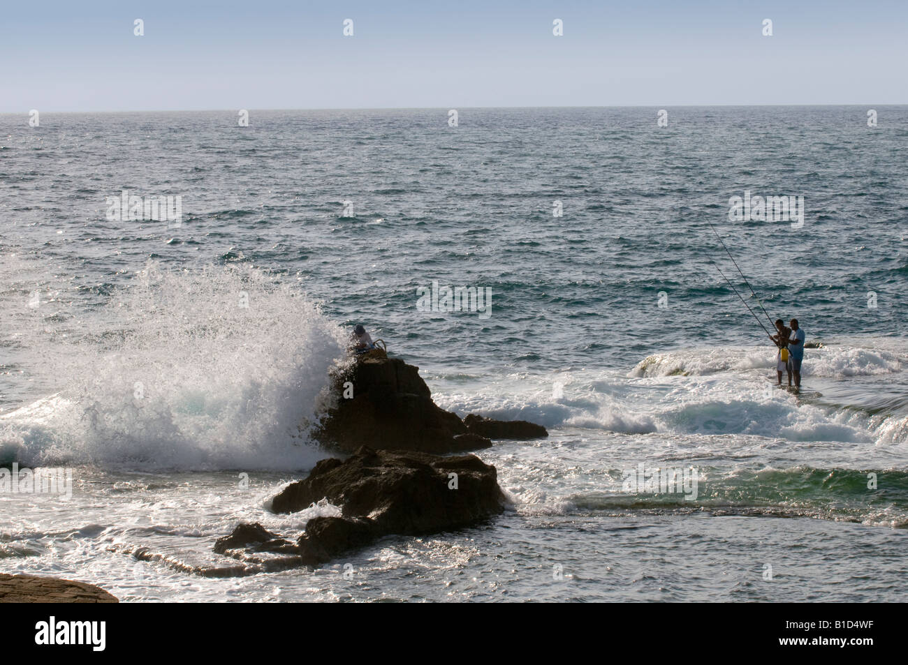 Les garçons la pêche sur les rochers dans la mer sont éclaboussés par les vagues de la marée montante, Acre, Israël, Akkao Banque D'Images