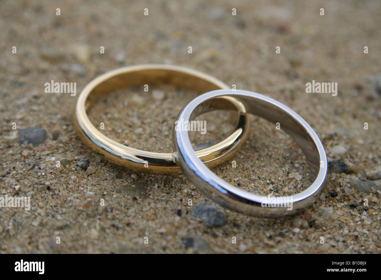 Gros plan de deux anneaux de mariage organisé sur une plage de sable Banque D'Images