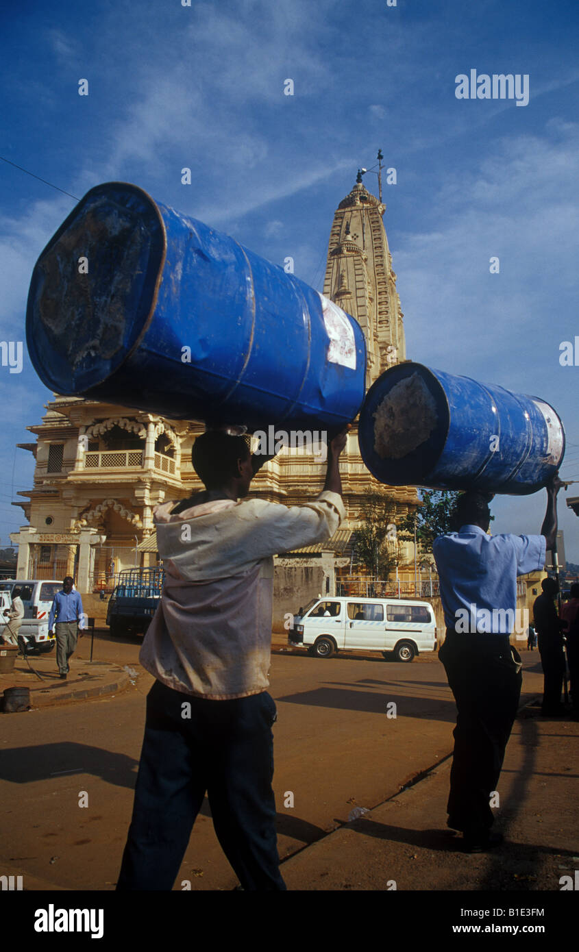 Deux hommes transportent le pétrole barils sur leurs têtes en face d'un temple hindou dans la capitale de l'Ouganda, Kampala. Banque D'Images