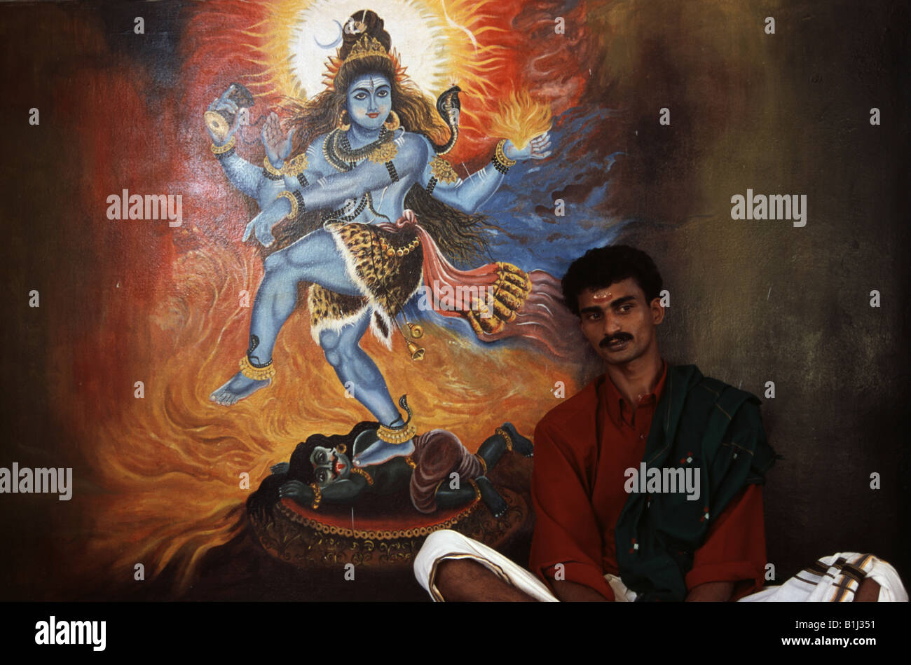 Prêtre assis en face d'une peinture de Seigneur Shiva dans un temple, Kerala, Inde Banque D'Images
