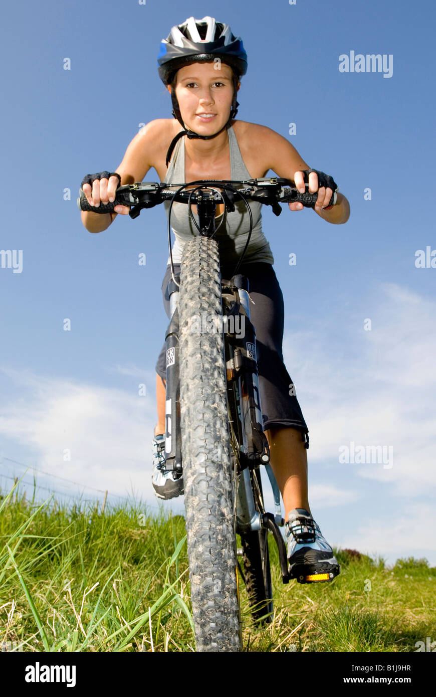 Jeune femme avec casque sur un VTT, passage sur un pré Banque D'Images