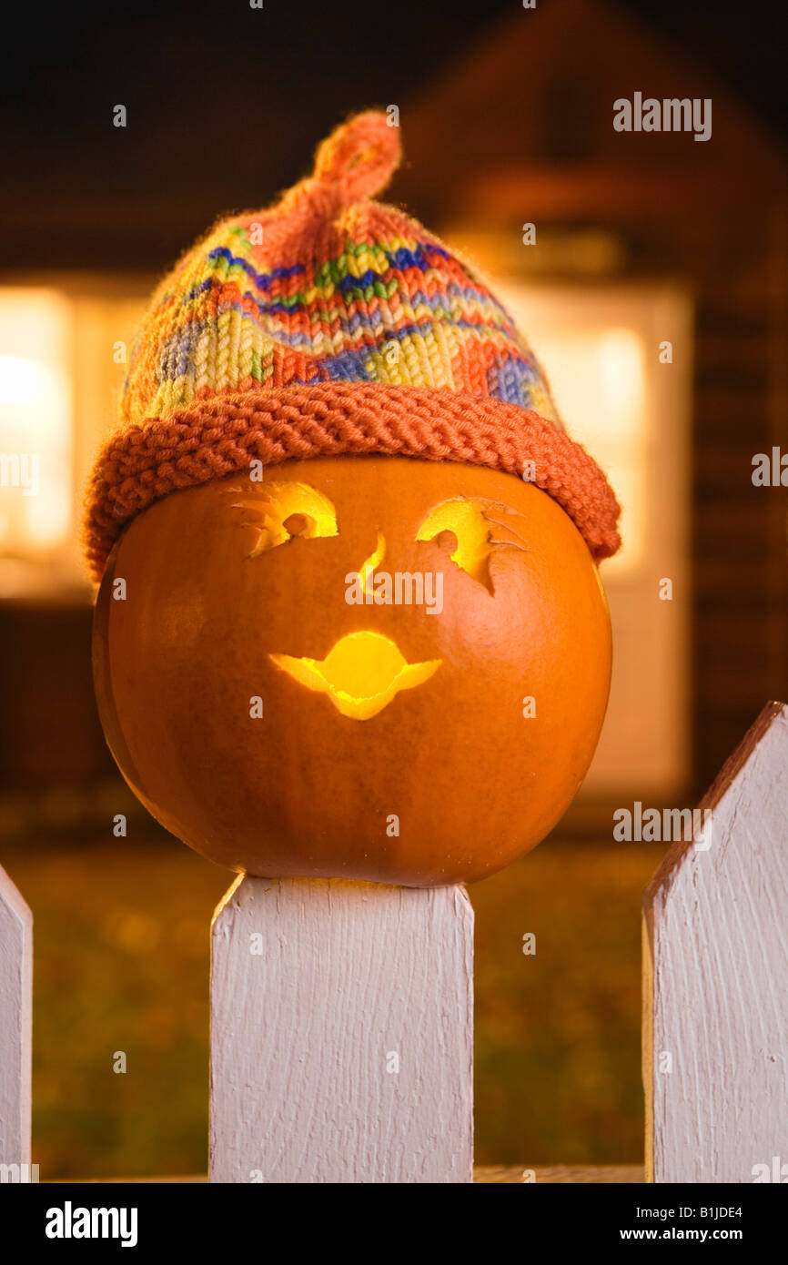 Jack-O-Lantern face portant un chapeau bas coincé au sommet d'un piquet de clôture blanche picktet au crépuscule au cours de l'automne Banque D'Images