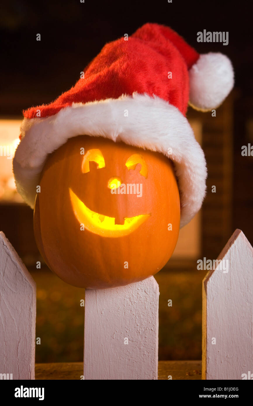 Jack-O-Lantern face wearing a santa hat coincé au sommet d'un piquet de clôture blanche picktet au crépuscule au cours de l'automne Banque D'Images