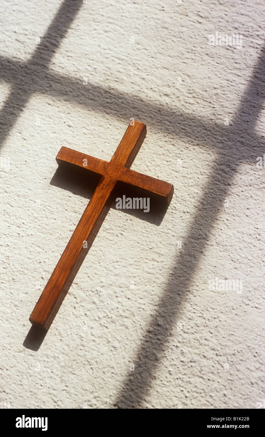 Close up of small crucifix en bois simple couché dans la lumière du soleil sur le rebord de la texture peint en blanc avec l'écho des ombres cross Banque D'Images