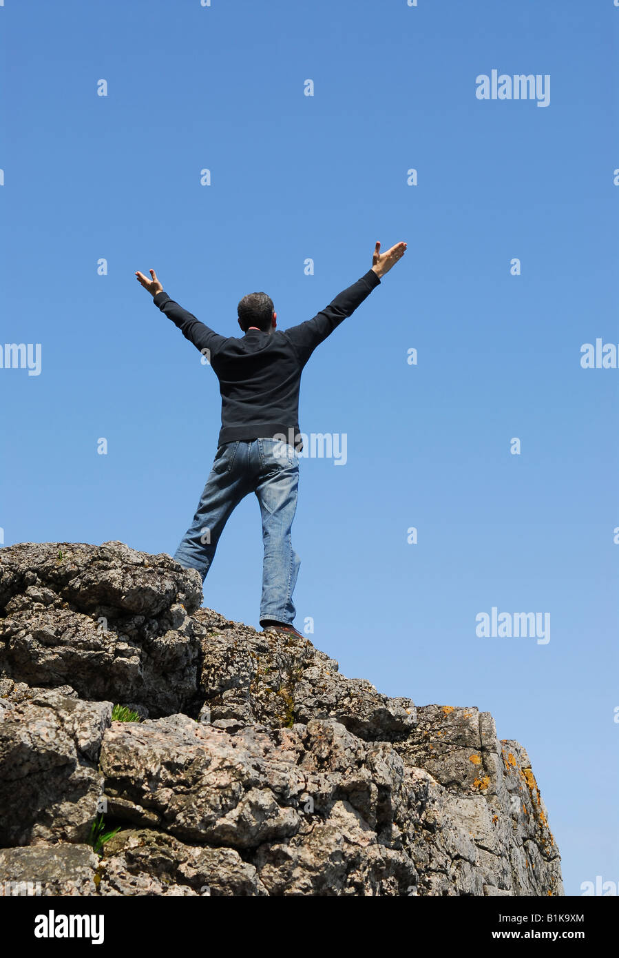 Un homme debout sur une falaise avec ses bras levés vers le ciel bleu Banque D'Images